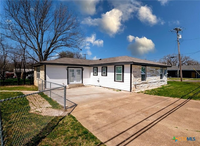 view of front facade featuring driveway, stone siding, fence, french doors, and a front yard