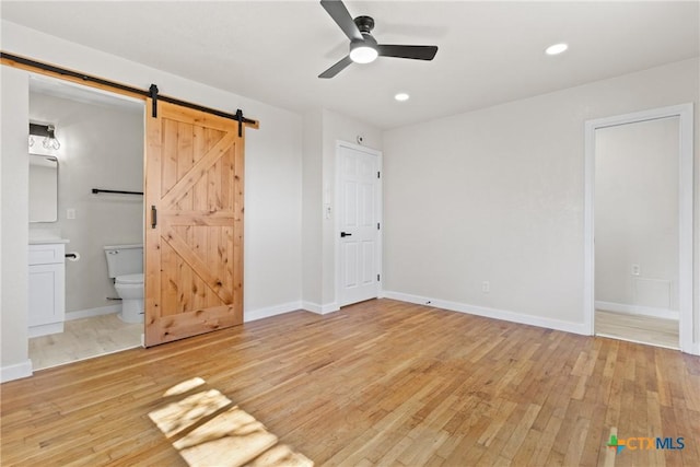 unfurnished bedroom with a barn door, recessed lighting, hardwood / wood-style floors, and baseboards