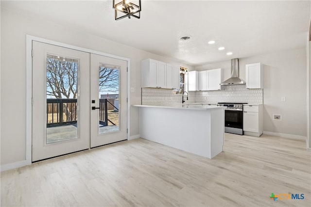 kitchen featuring stainless steel range oven, wall chimney exhaust hood, white cabinetry, and light countertops