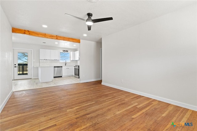 unfurnished living room with a ceiling fan, a sink, light wood-style flooring, and baseboards