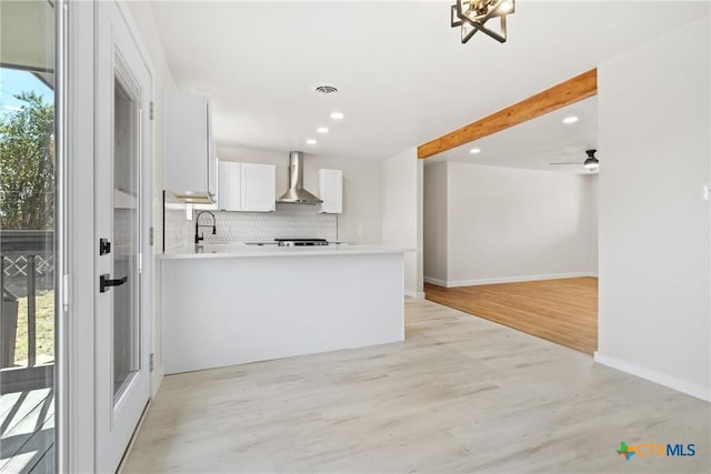 kitchen featuring light countertops, decorative backsplash, white cabinetry, wall chimney range hood, and a peninsula