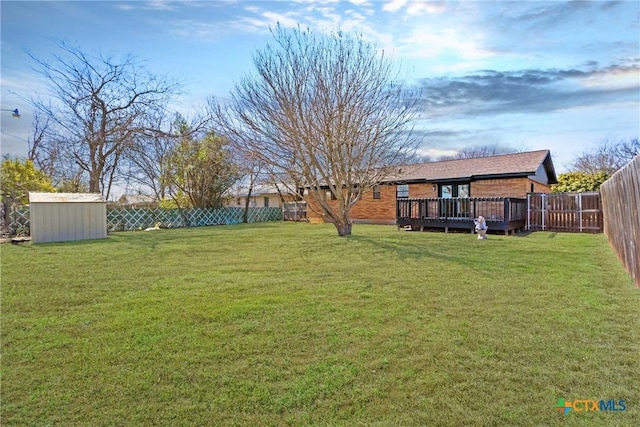 view of yard featuring an outbuilding, a fenced backyard, a wooden deck, and a storage unit