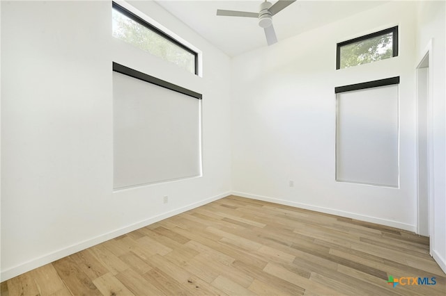 spare room featuring a high ceiling, light wood-type flooring, and ceiling fan