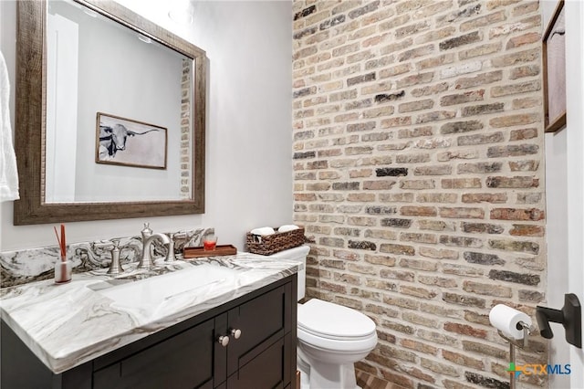 bathroom featuring brick wall, toilet, and vanity