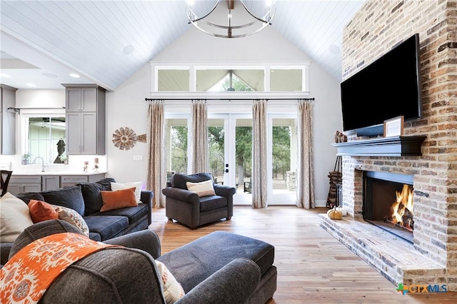 living room with high vaulted ceiling, sink, light hardwood / wood-style floors, and a brick fireplace