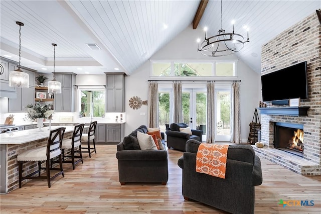 living room with high vaulted ceiling, a chandelier, light hardwood / wood-style floors, a brick fireplace, and wooden ceiling