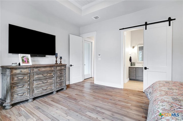 bedroom featuring crown molding, ensuite bathroom, a raised ceiling, a barn door, and light wood-type flooring