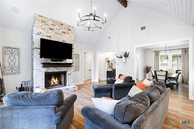 living room with an inviting chandelier, a brick fireplace, high vaulted ceiling, and light hardwood / wood-style flooring