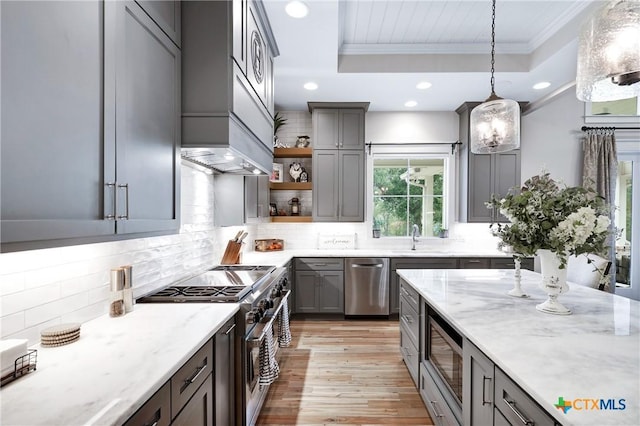 kitchen featuring a raised ceiling, hanging light fixtures, ornamental molding, light stone counters, and stainless steel appliances