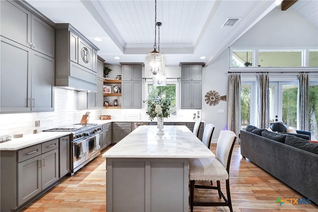 kitchen with gray cabinetry, hanging light fixtures, a kitchen island, stainless steel appliances, and light hardwood / wood-style floors