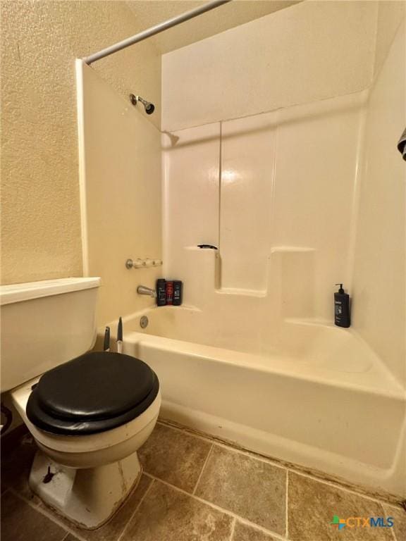 full bath featuring tile patterned flooring, washtub / shower combination, a textured wall, and toilet