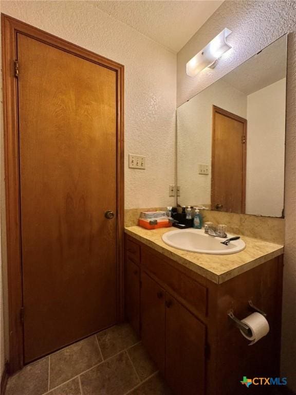 bathroom featuring a textured ceiling, a textured wall, and vanity