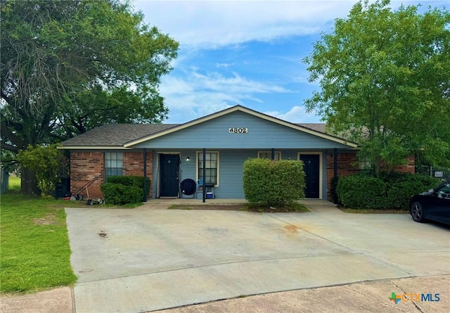 ranch-style home featuring covered porch, brick siding, and a front yard