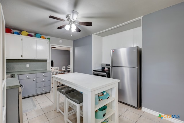 kitchen with ceiling fan, light tile patterned floors, a kitchen bar, white cabinets, and appliances with stainless steel finishes