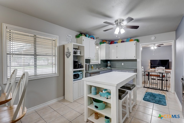 kitchen featuring a breakfast bar, ceiling fan, sink, light tile patterned floors, and white cabinets