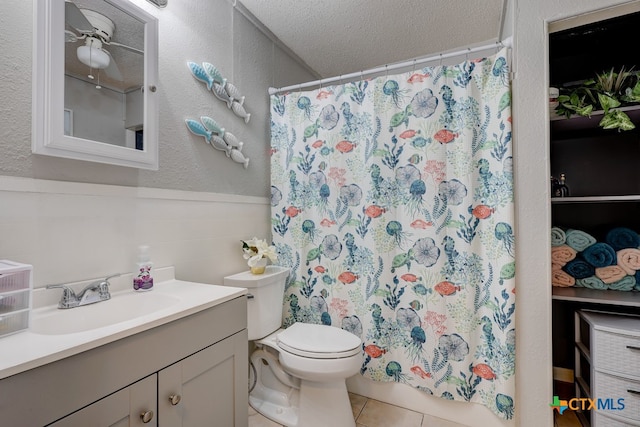 bathroom with ceiling fan, tile patterned flooring, a textured ceiling, toilet, and vanity