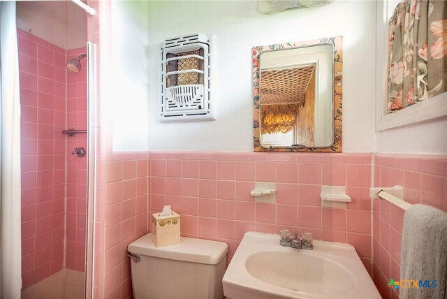 bathroom featuring a stall shower, a wainscoted wall, toilet, a sink, and tile walls