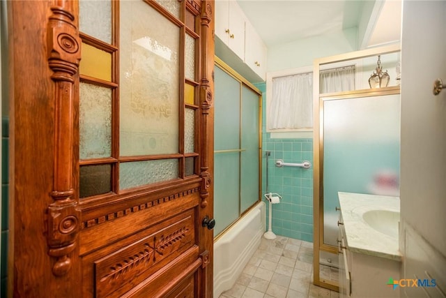 full bath with tile walls, enclosed tub / shower combo, tile patterned floors, and vanity