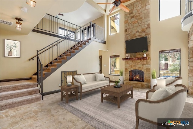 living room featuring a high ceiling, a stone fireplace, and ceiling fan