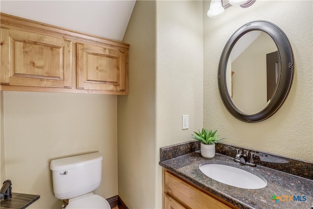 bathroom with vanity, toilet, and lofted ceiling