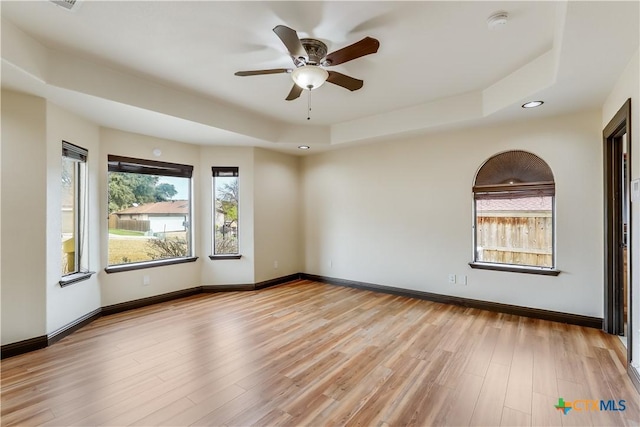 spare room with light hardwood / wood-style floors, a raised ceiling, and ceiling fan