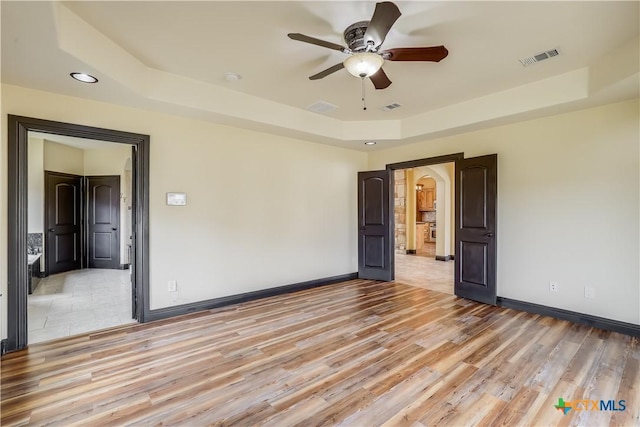 unfurnished room featuring light hardwood / wood-style floors, a raised ceiling, and ceiling fan