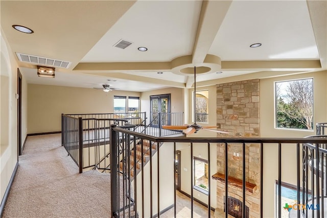 corridor featuring beam ceiling, a wealth of natural light, and light carpet