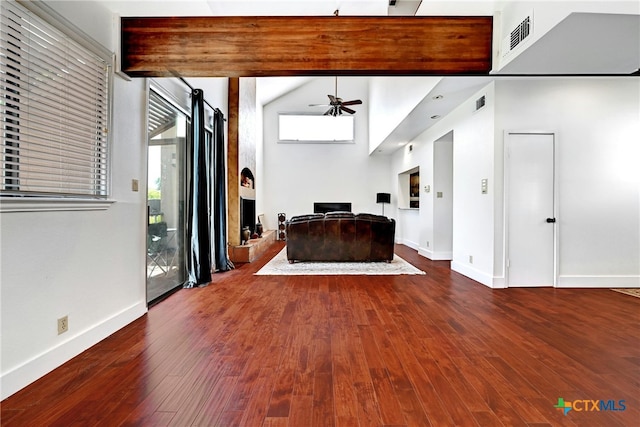 unfurnished living room featuring beam ceiling, hardwood / wood-style floors, ceiling fan, and a towering ceiling