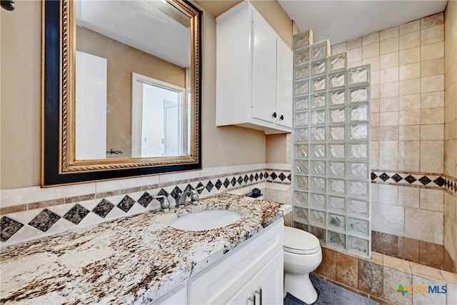 bathroom featuring vanity, toilet, a tile shower, and tile walls