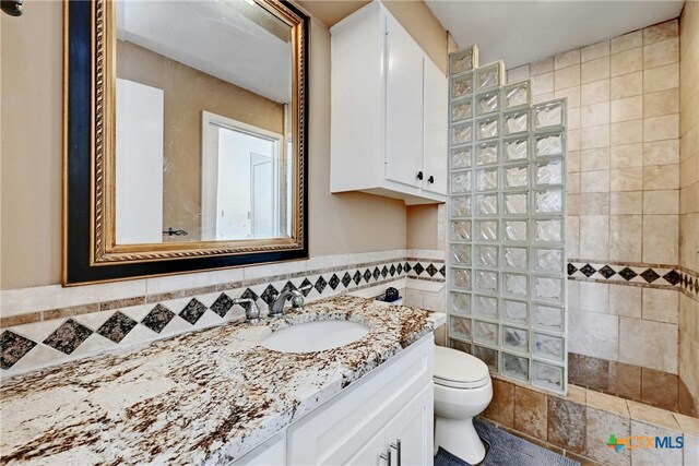 bathroom featuring vanity, toilet, a tile shower, and tile walls