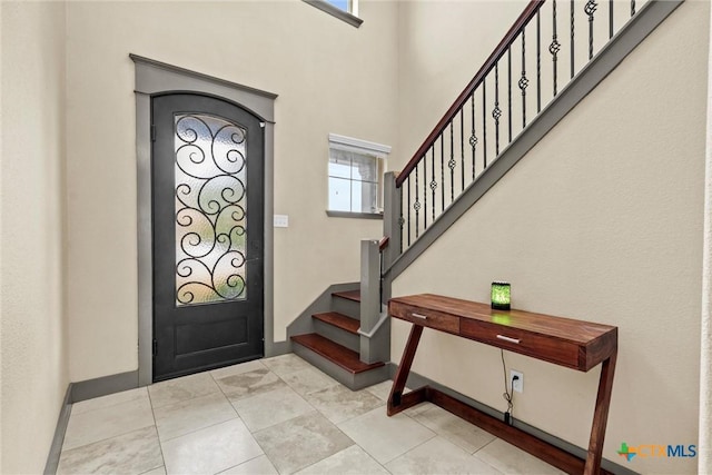 foyer entrance featuring a towering ceiling, baseboards, and stairs