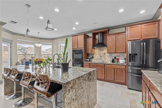 kitchen featuring light stone counters, wall chimney range hood, black appliances, tasteful backsplash, and brown cabinetry