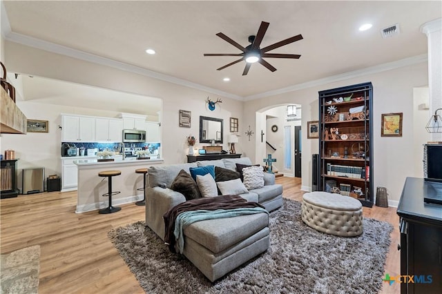 living room with ceiling fan, crown molding, and light wood-type flooring