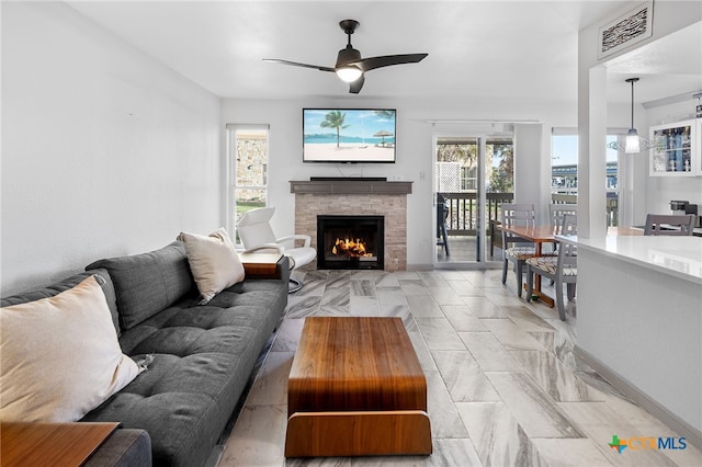 living area with baseboards, a fireplace, visible vents, and ceiling fan