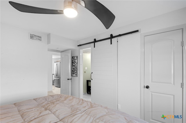 bedroom with visible vents, a barn door, ceiling fan, and freestanding refrigerator