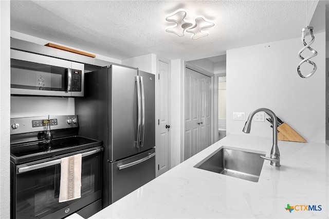 kitchen with a sink, a textured ceiling, and stainless steel appliances