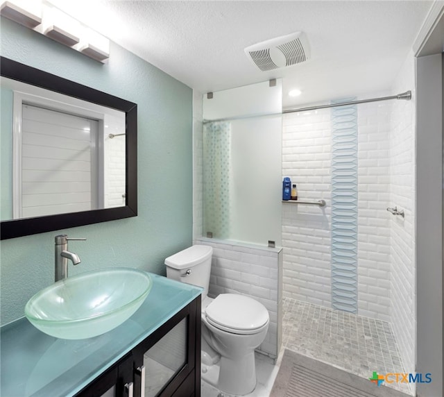 bathroom featuring visible vents, toilet, tiled shower, and vanity