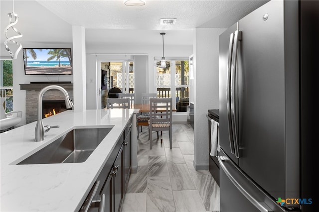 kitchen featuring a sink, decorative light fixtures, light stone counters, a warm lit fireplace, and freestanding refrigerator