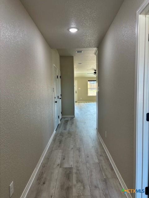 hallway with a textured ceiling and light wood-type flooring