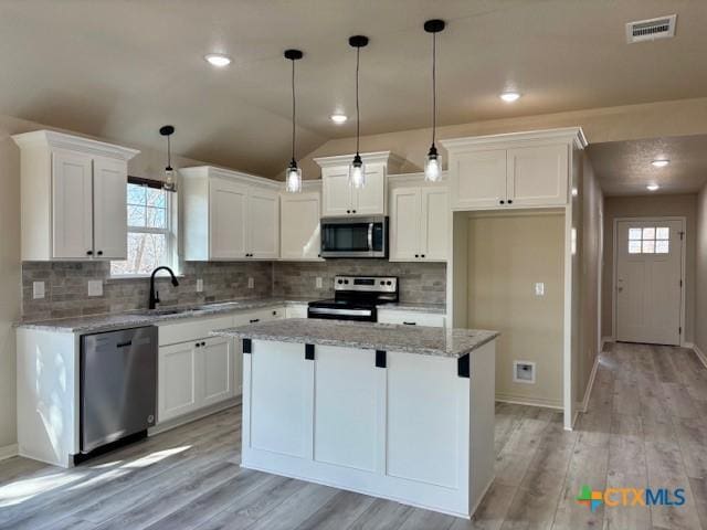 kitchen with light stone countertops, appliances with stainless steel finishes, lofted ceiling, a kitchen island, and white cabinetry