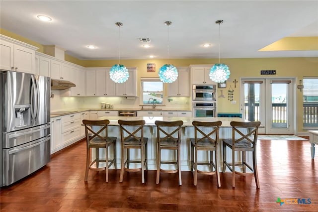 kitchen featuring visible vents, dark wood finished floors, a kitchen bar, white cabinets, and stainless steel appliances