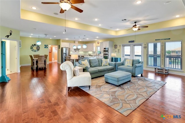 living room with visible vents, a ceiling fan, a tray ceiling, hardwood / wood-style floors, and baseboards