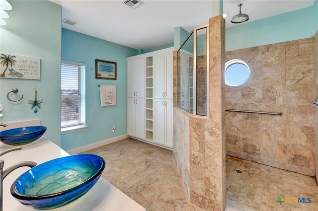 bathroom with visible vents, baseboards, walk in shower, double vanity, and a sink