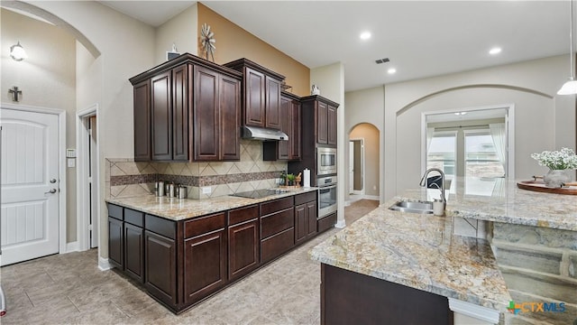 kitchen with a sink, under cabinet range hood, arched walkways, appliances with stainless steel finishes, and decorative backsplash
