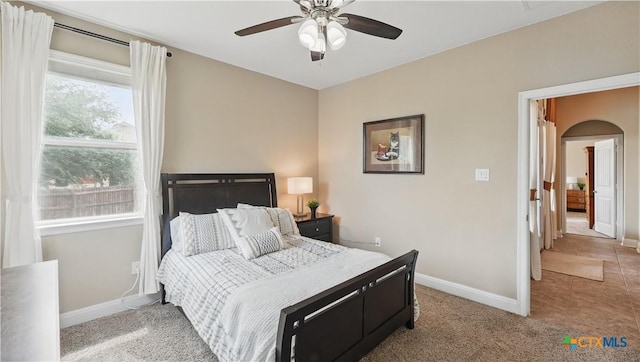 carpeted bedroom featuring arched walkways, baseboards, and a ceiling fan