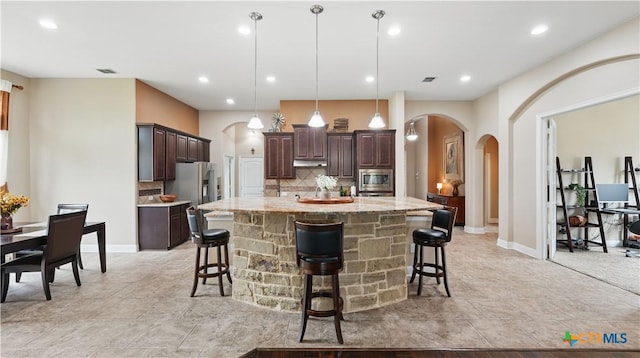 kitchen featuring arched walkways, tasteful backsplash, dark brown cabinetry, a kitchen breakfast bar, and appliances with stainless steel finishes