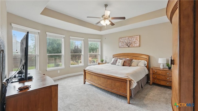 bedroom with light carpet, multiple windows, baseboards, and a raised ceiling