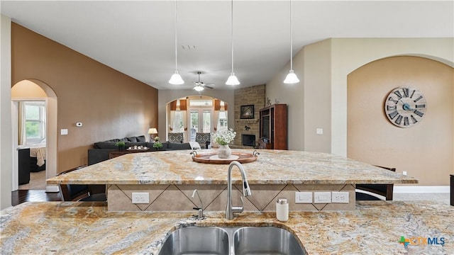 kitchen with arched walkways, a sink, light stone counters, and decorative light fixtures