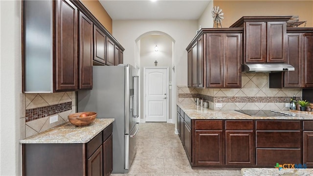 kitchen featuring under cabinet range hood, arched walkways, stainless steel fridge with ice dispenser, black electric stovetop, and dark brown cabinets