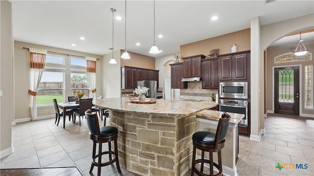 kitchen with appliances with stainless steel finishes, arched walkways, backsplash, dark brown cabinetry, and a breakfast bar